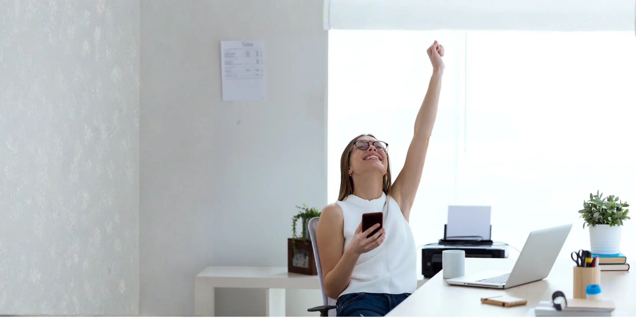 Agente de seguros celebrando en su escritorio con el teléfono en la mano