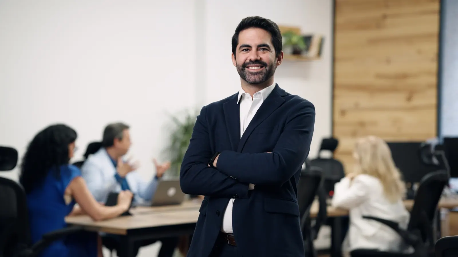 Agente de seguros de pie en una oficina donde su equipo trabaja al fondo