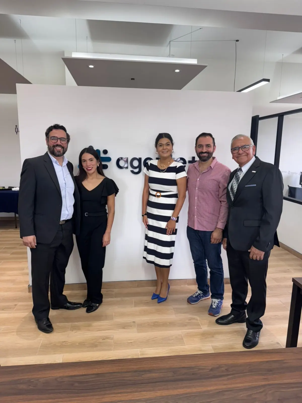 Cinco integrantes del equipo de Agente Más posando frente al logotipo en la recepción de la oficina